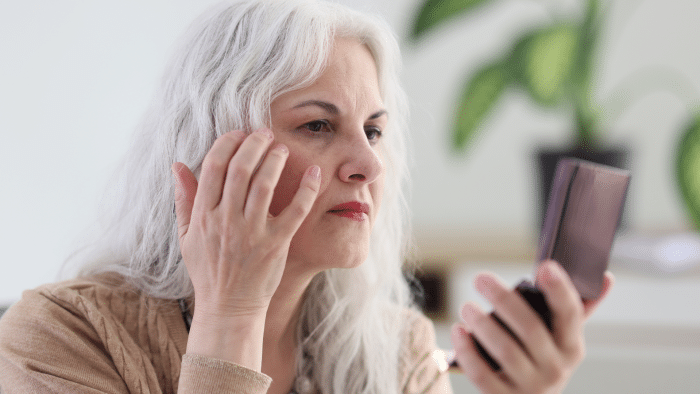 Older woman feeling troubled over visible signs of aging on her skin.