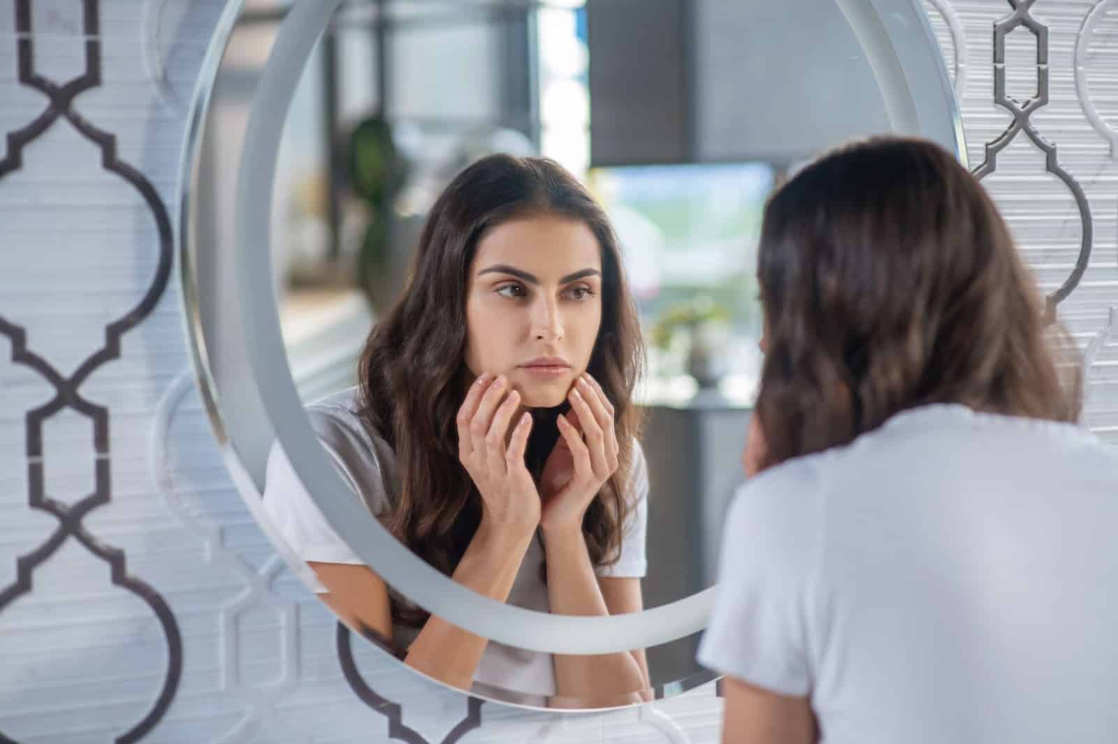 Woman examining her face in the mirror.