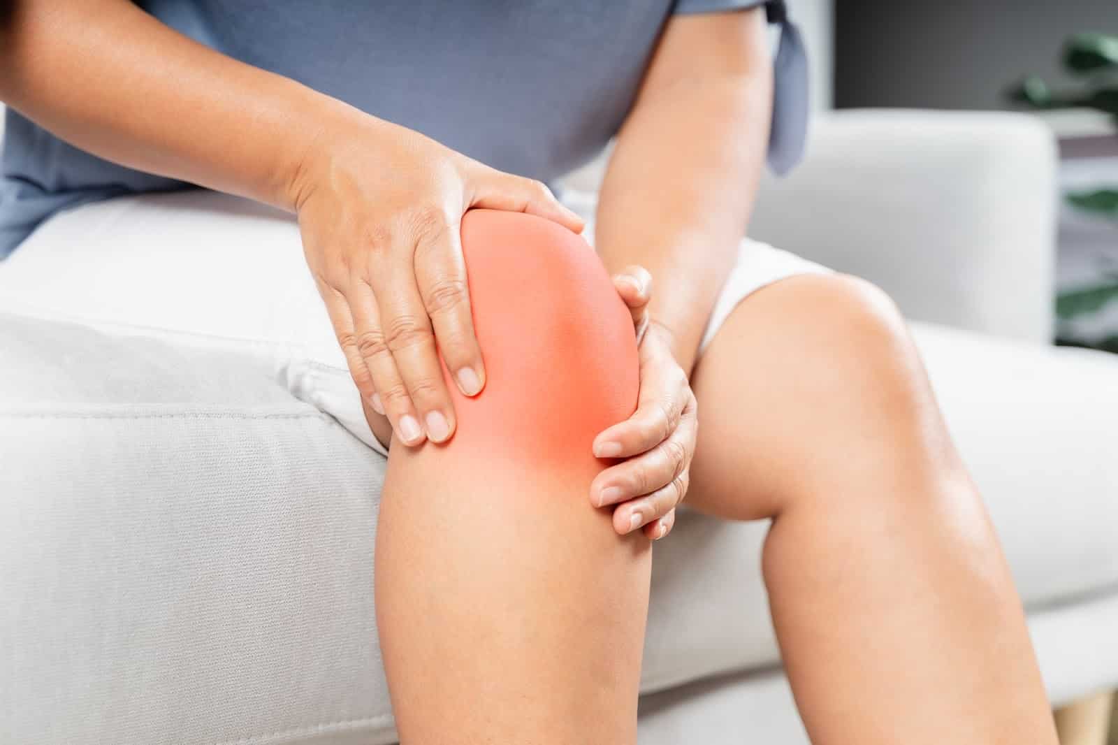 Woman sitting down on the couch and cradling the knee after feeling pain.