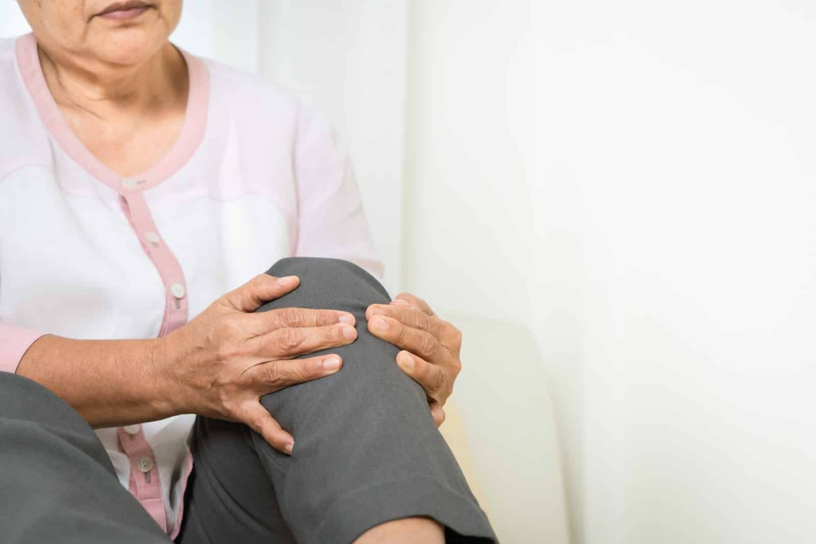 A senior woman clutching her knee joint after feeling pain.