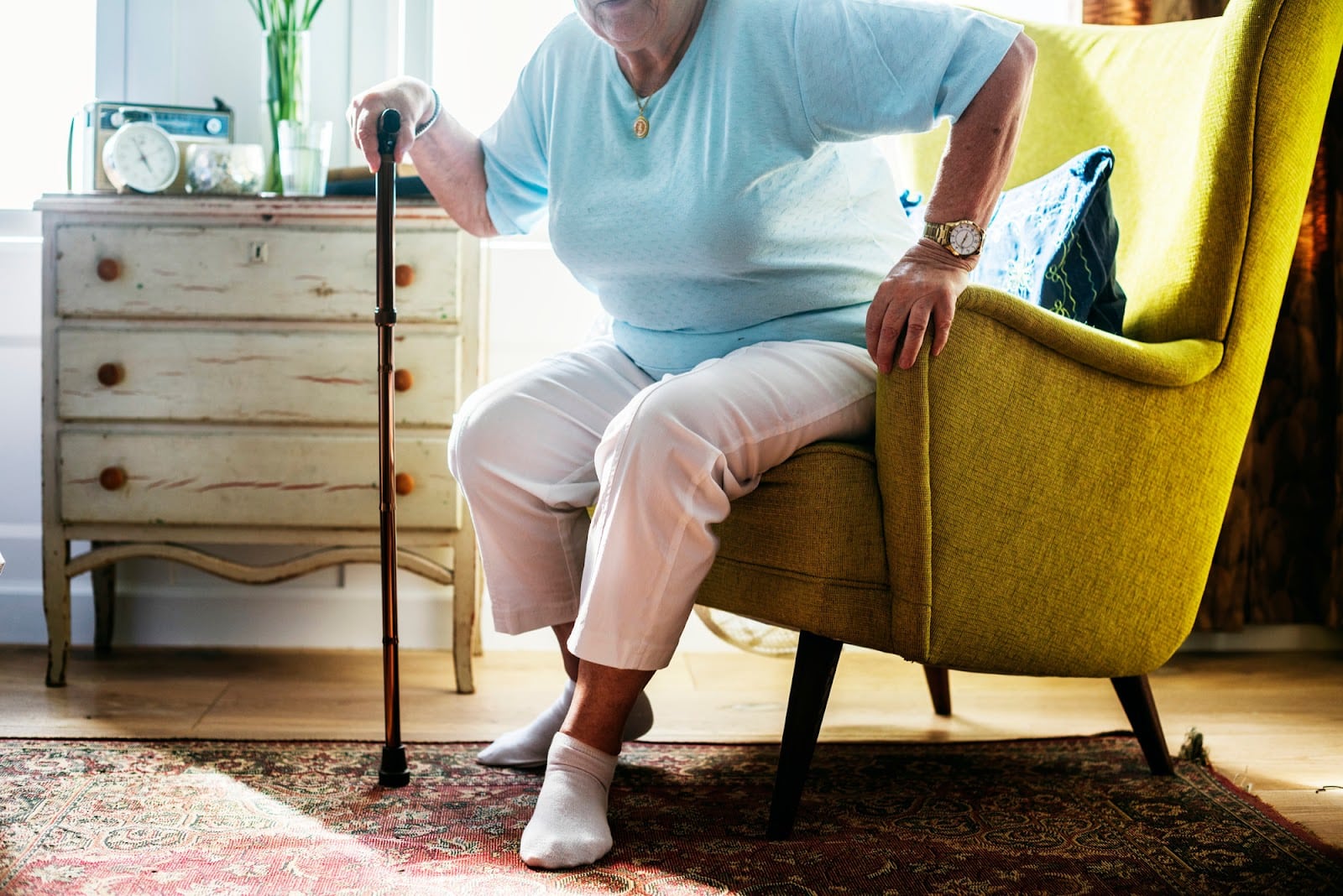 A senior woman struggling to stand up from her chair because of osteoarthritis in the knee.