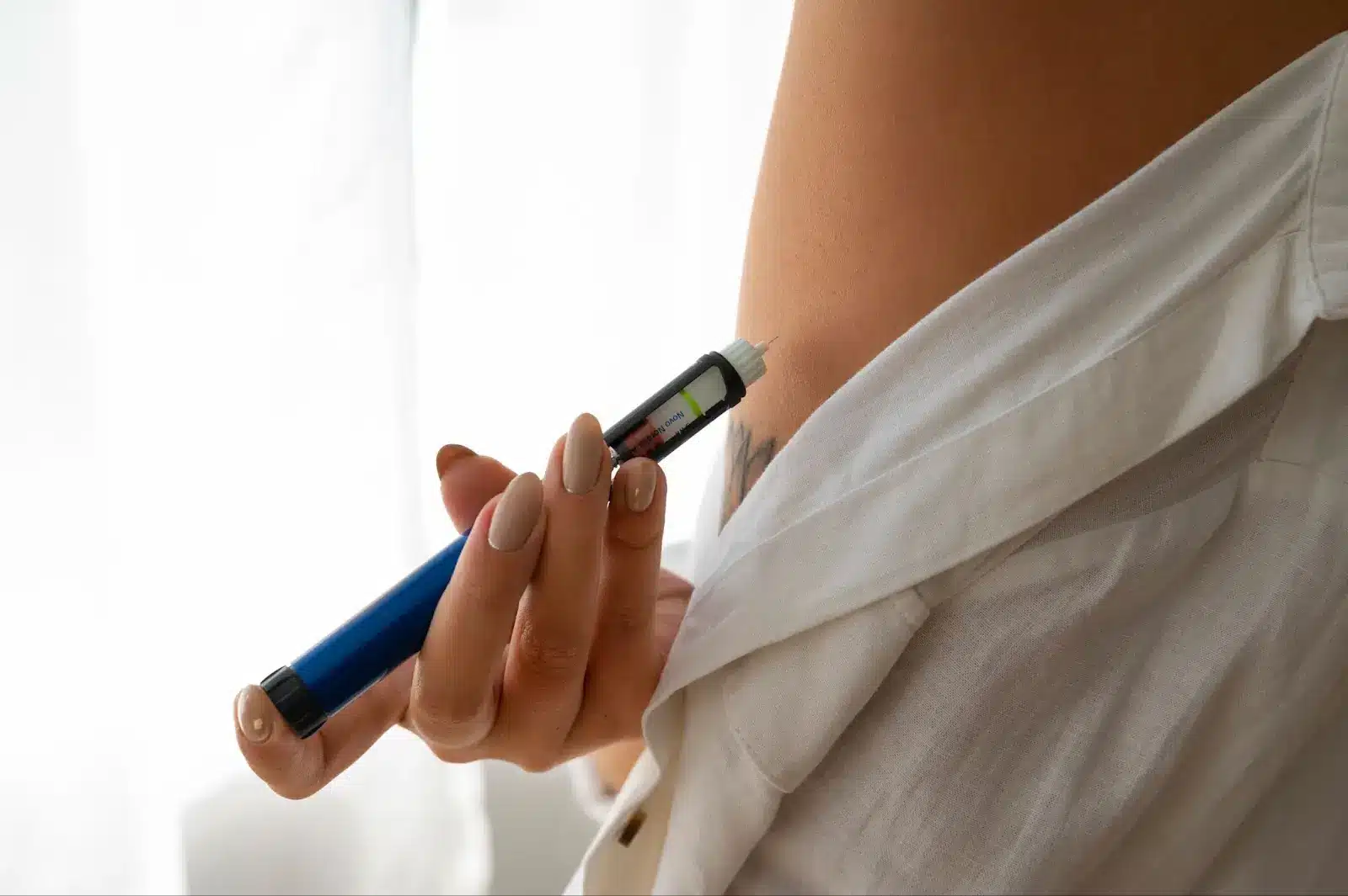 A person that is holding an injection that is similar to Mounjaro near her arm. The background is white. 