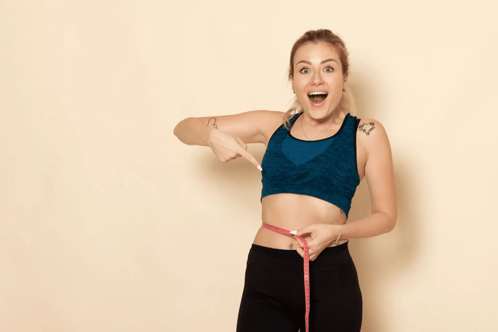 A female who is pointing at the measuring tape wrapped around her waist. She looks happy. The background is yellow. 